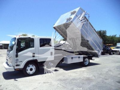 Isuzu NPR-HD dump truck with raised aluminum dump body in a truck yard.