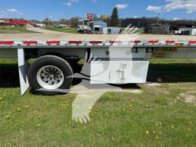 Flatbed trailer side view showing wheel well and undercarriage chrome toolbox with Maxmiser branding plate. Reflective tape along edge and grassy area.
