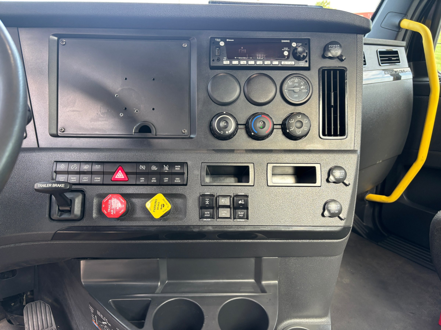 Cab dashboard of a Freightliner truck showing instrumentation cluster, climate controls, hazard button, and various switches.