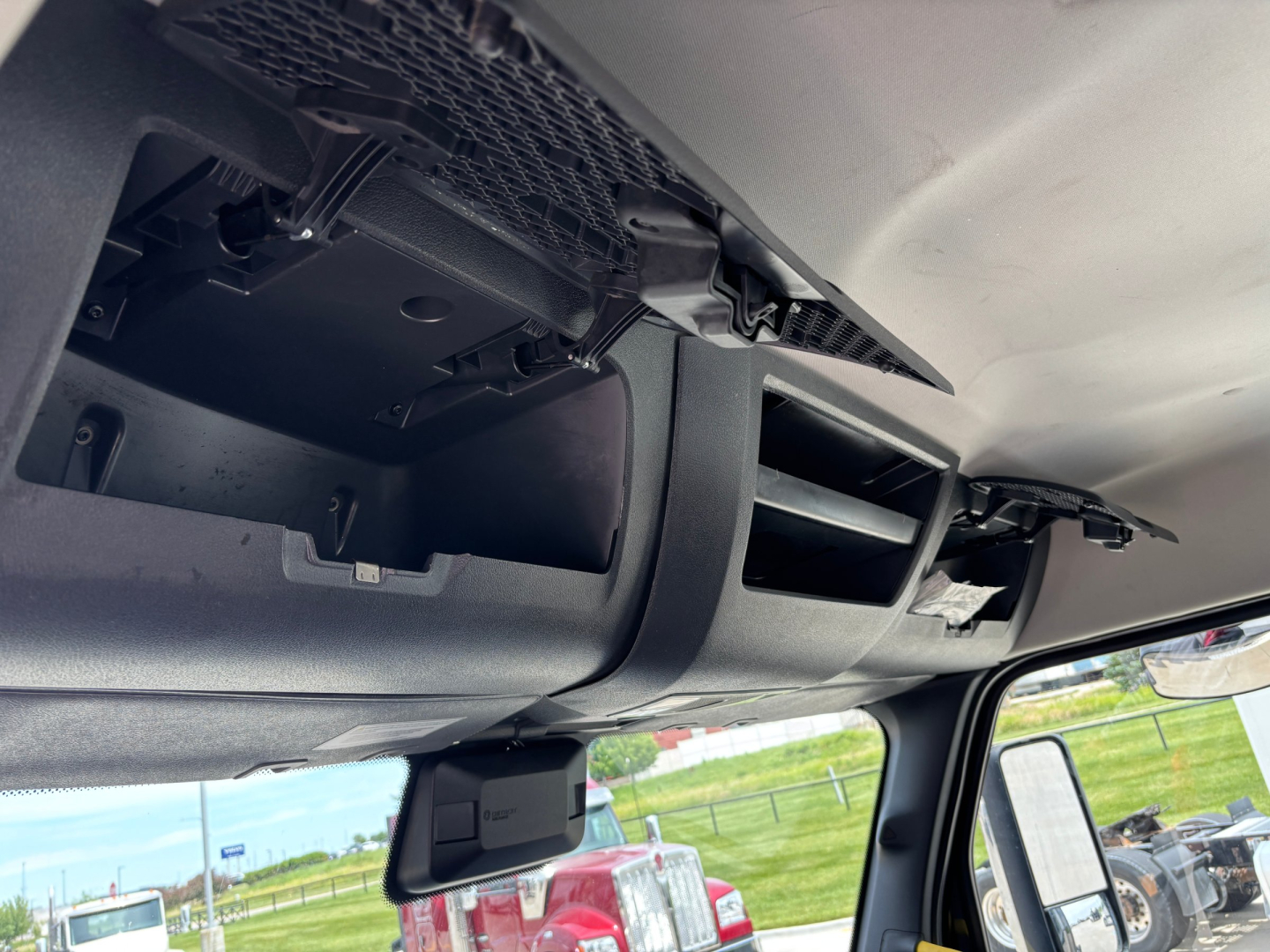 Vehicle interior front dash area of a Freightliner daycab showing vents and storage compartment under the dash.