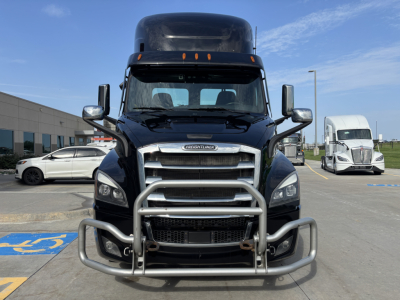 Front view of a Freightliner truck with a heavy-duty grille guard, chrome mirrors, and prominent bumper in a parking lot.
