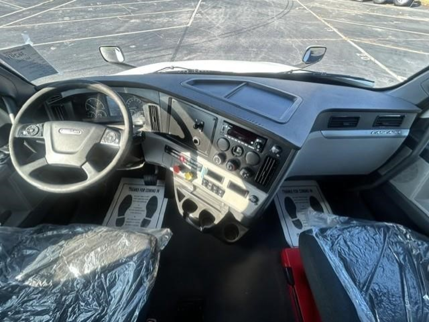 Freightliner Cascadia 126 interior dashboard and steering wheel view with center console and seats covered in protective plastic.