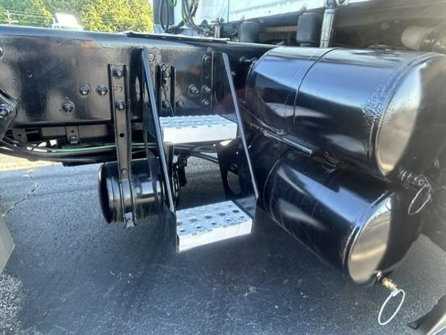 Freightliner Cascadia 126 undercarriage with metal step ladder and cylindrical fuel tanks; visible chrome steps and black chassis with mounting brackets.