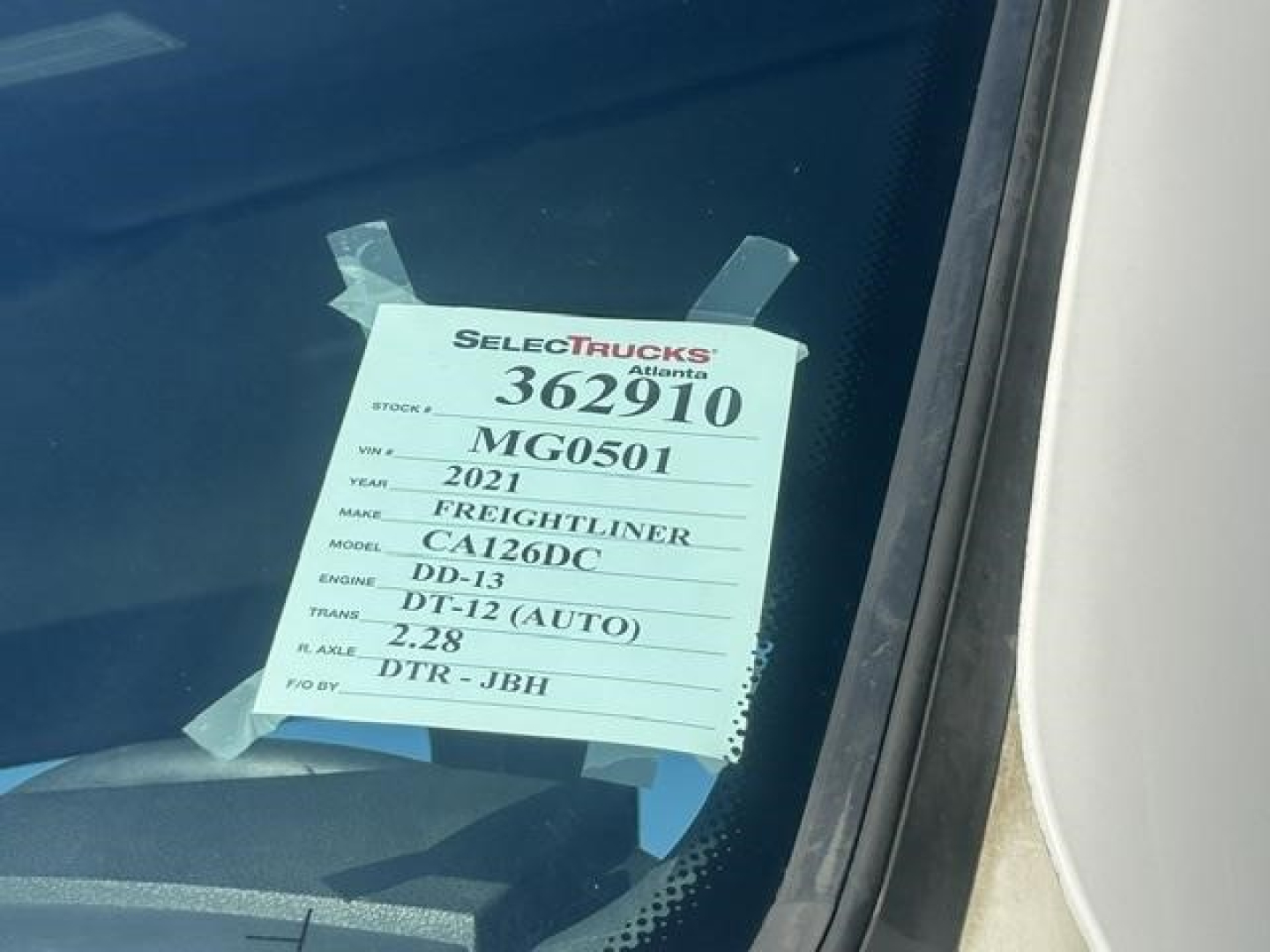 Truck dealer tag on windshield showing 2021 Freightliner Cascadia 126 with stock 362910, model CA126DC, DD-13 engine, automatic DDT-12, 2.28 axle ratio.