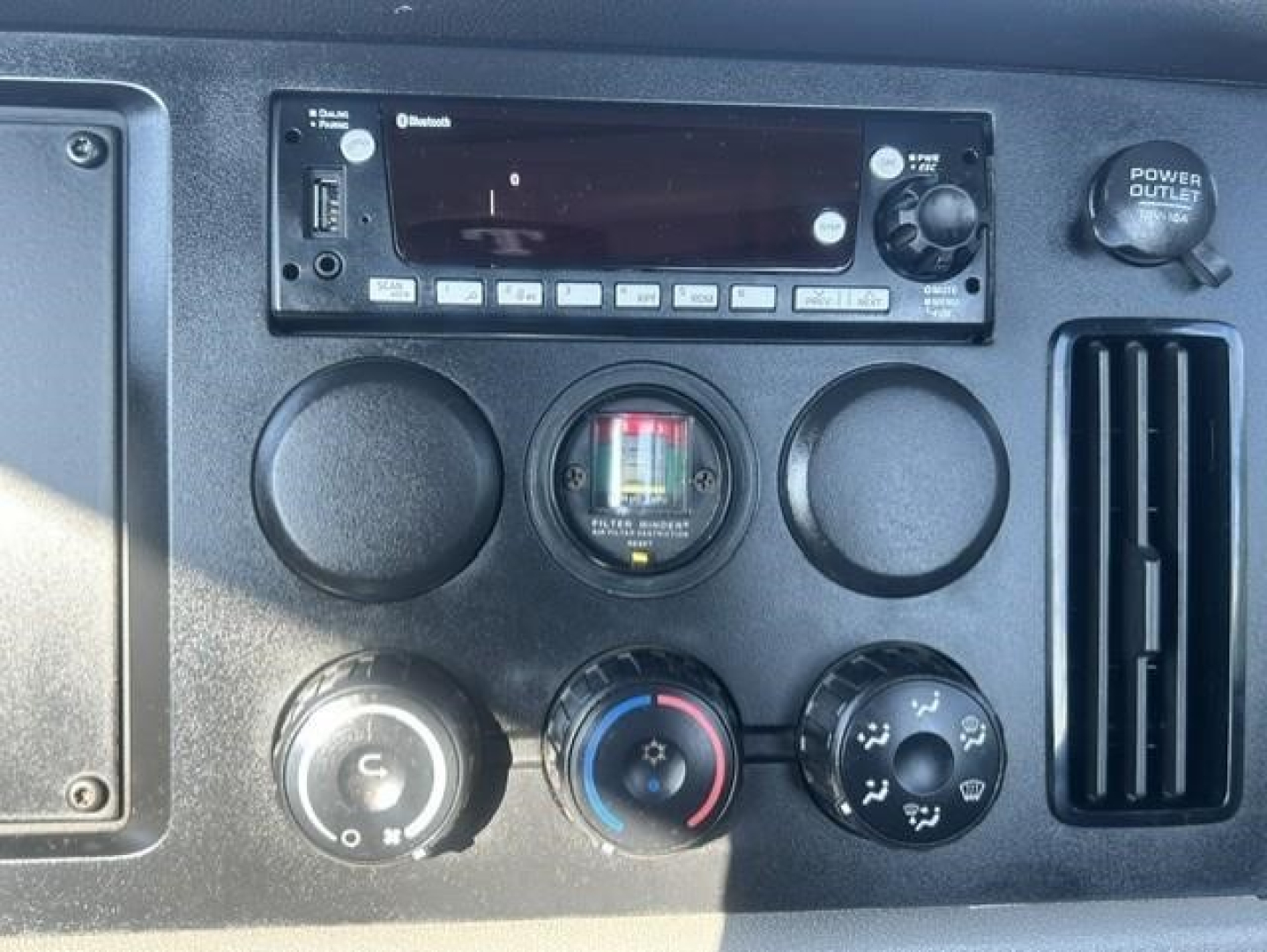 Dashboard controls of a Freightliner Cascadia Day Cab showing radio head unit, gauges, climate controls, power outlet, and vents.