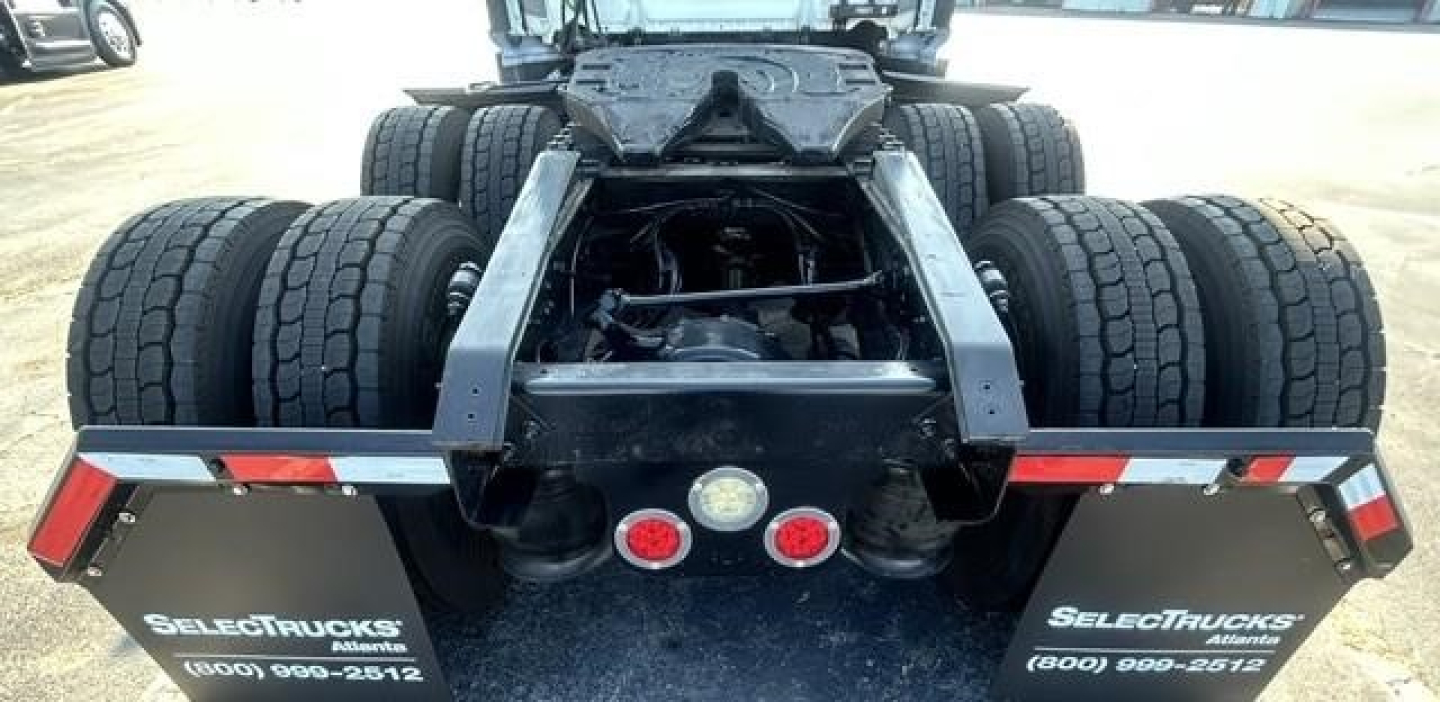 Rear view of a Freightliner Cascadia chassis showing dual rear axles and fifth wheel area. Dual rear tires on both drive axles visible; mud flaps with SELECT TRUCKS branding and contact numbers.