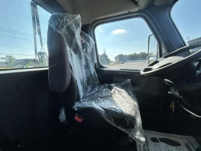 Truck cab interior showing driver's seat wrapped in plastic and steering wheel; window and dashboard visible.