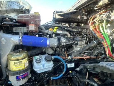 Freightliner Cascadia 126 engine bay showing blue coolant hose, air filter canister, and various wires and reservoirs.