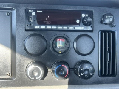 Dashboard controls of a Freightliner Cascadia Day Cab showing radio head unit, gauges, climate controls, power outlet, and vents.