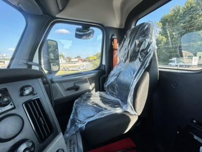Cab interior of a Freightliner Cascadia day cab showing plastic-covered seat and dashboard controls.