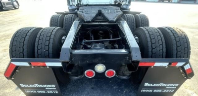 Rear view of a Freightliner Cascadia chassis showing dual rear axles and fifth wheel area. Dual rear tires on both drive axles visible; mud flaps with SELECT TRUCKS branding and contact numbers.