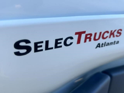 Service label on Freightliner Cascadia truck showing 'SELEC TRUCKS Atlanta' emblem and partial blue vehicle edge.