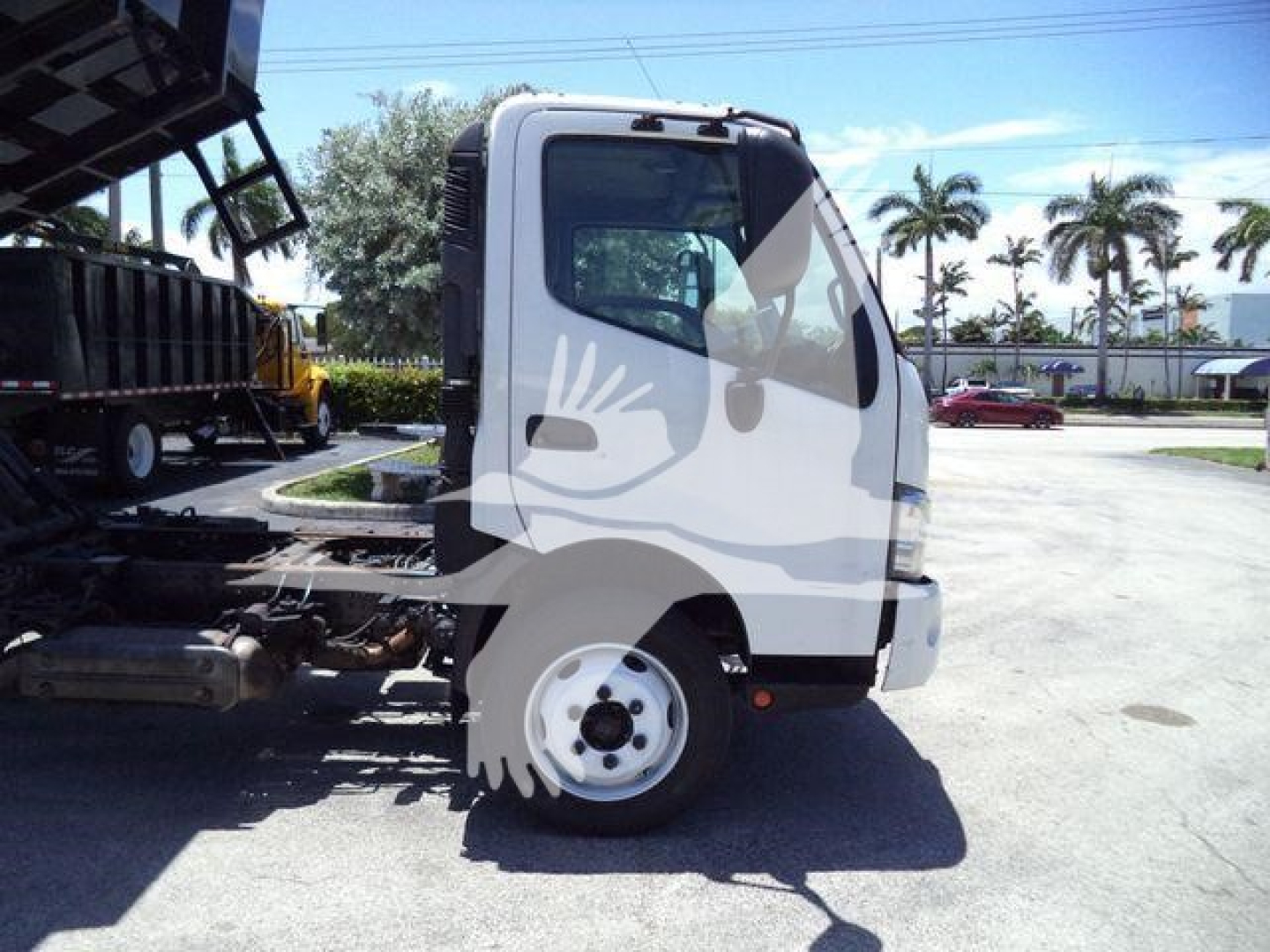 Truck cab side view showing front wheel and chassis of a 2020 Hino 195 dump truck with cab-over design.