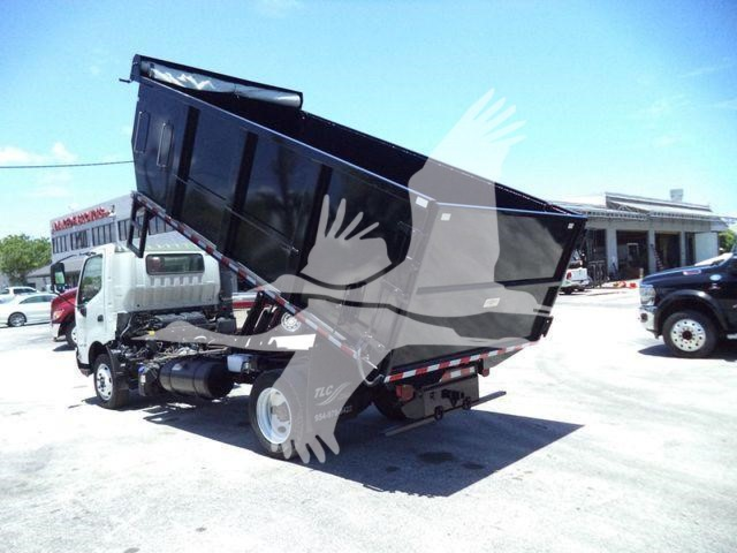 Dump truck bed tilted up showing cargo bed with hydraulic lift and Hino cab; VIN tag not visible; dealership lot.