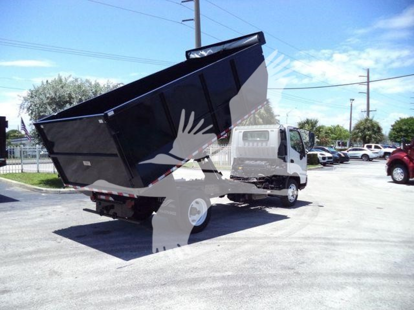 Truck with raised dump bed showing Hino 195 style cab and black dump body in a parking lot.