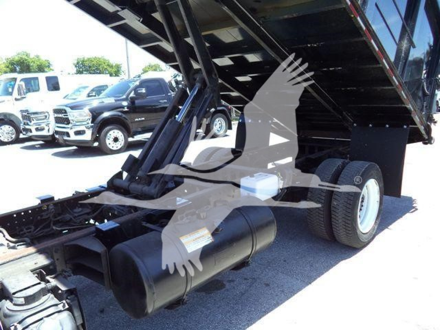 Truck dump bed with hydraulic system; visible components include a black cylindrical air tank and chassis; raised bed showing hydraulic mechanism and dual rear wheels.