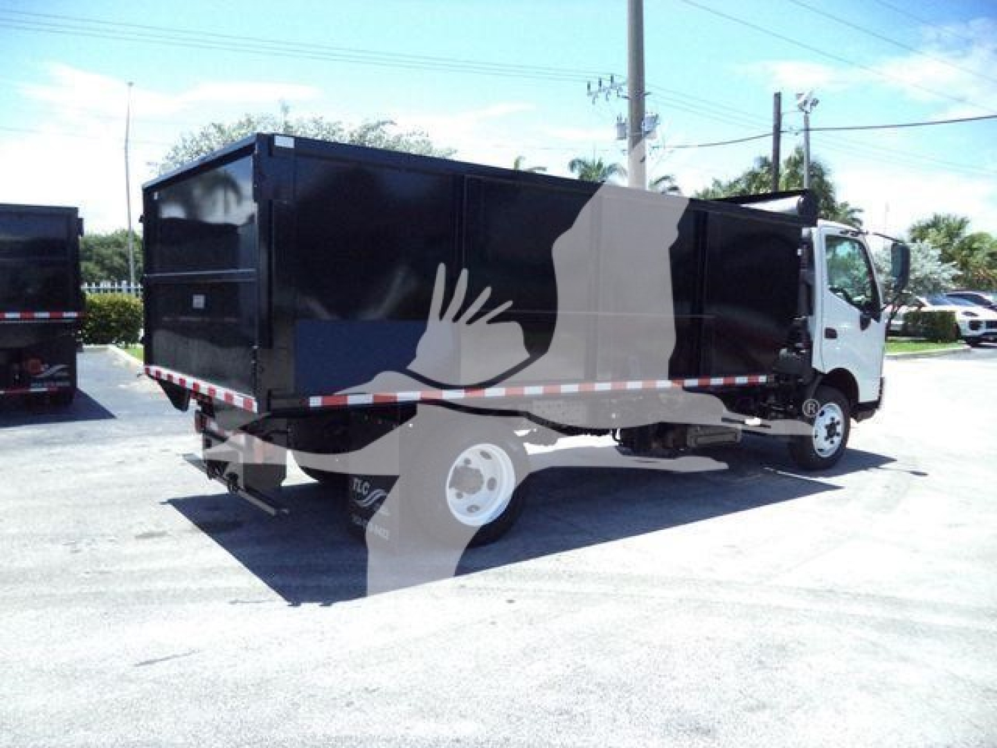 Dump truck with black dump body and white cab, side view, with reflective tape along the lower edge.