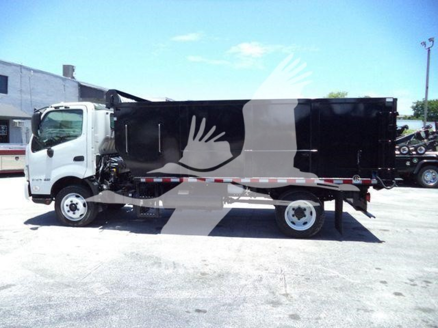 Hino 195 dump truck side view showing black dump body and white cab with stock number T02042 and VIN JHHGDM2H9LK002042