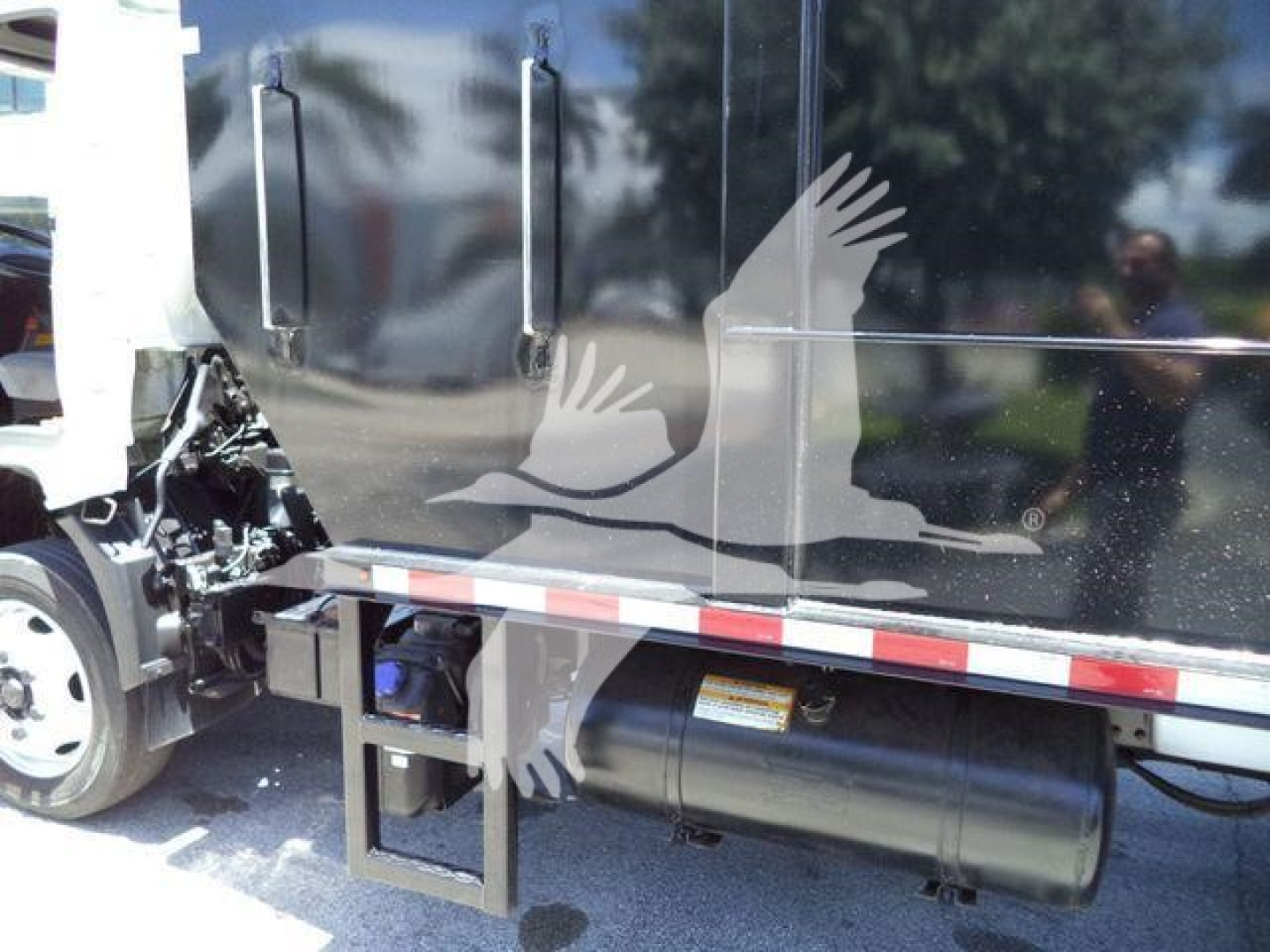 Truck side view showing black dump body with steps and cylindrical fuel tank beneath along with front wheel and door handle visible.