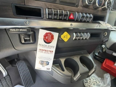 Western Star truck interior dash area showing trailer brake switch and control panel with hanging inspection tag and cup holders.