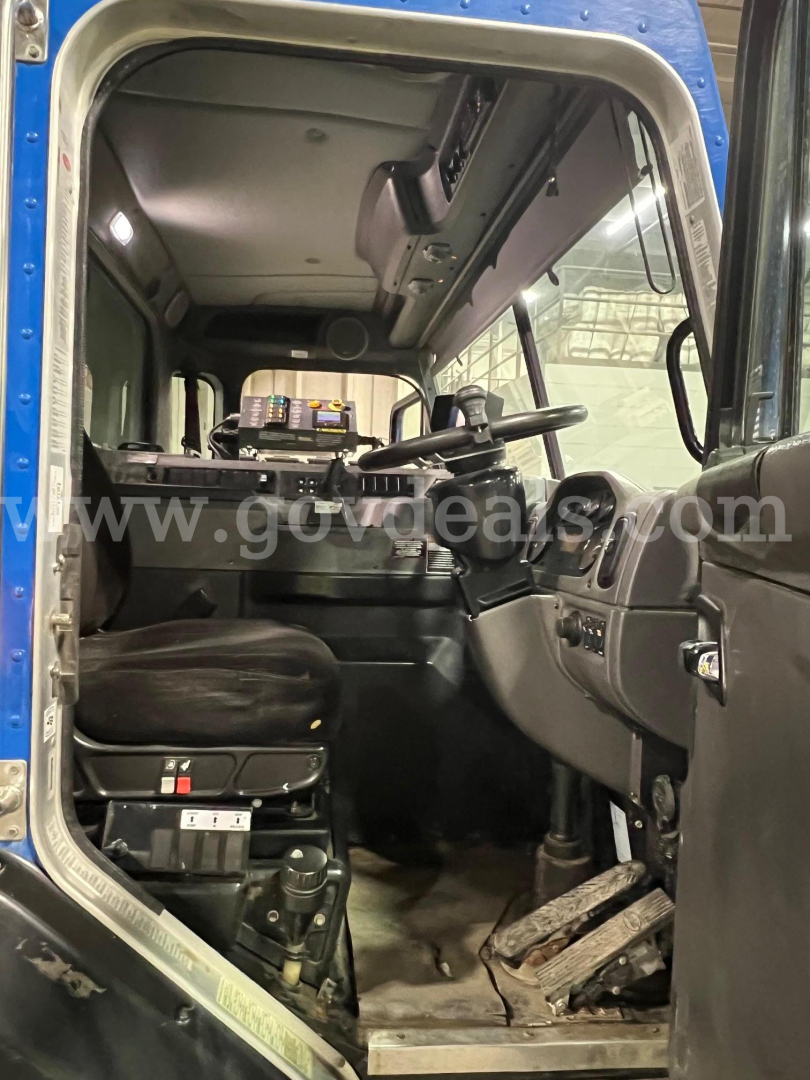 Cab interior of a 2016 Peterbilt 320 truck showing the driver's seat, steering wheel, dashboard, pedals, and overhead console.