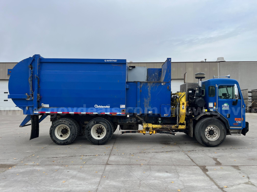 Peterbilt 320 garbage truck in blue with rear compactor and dual rear axles, side view showing cab and compactor mechanism.