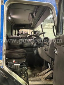 Cab interior of a 2016 Peterbilt 320 truck showing the driver's seat, steering wheel, dashboard, pedals, and overhead console.