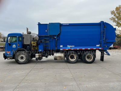Peterbilt 320 dump truck side view showing large blue rear cargo bed and cab; various hoses and compartments under cab; stock number 4677-227 plate area visible.