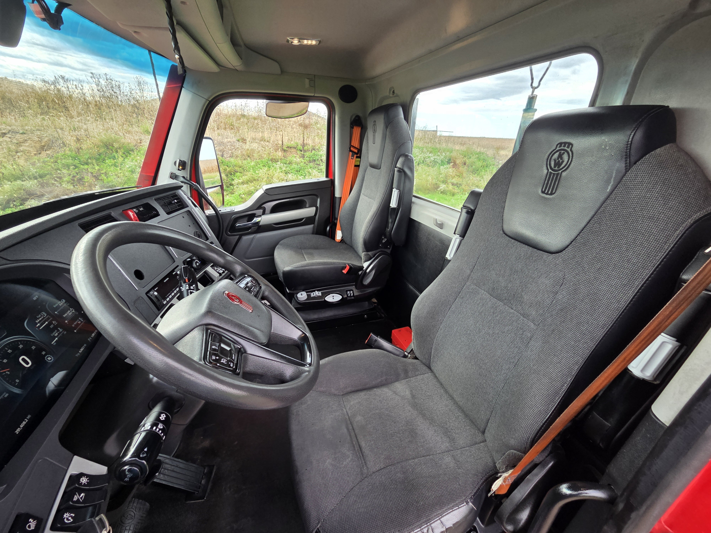 Kenworth T680 truck cab interior showing driver's seat and passenger seat with steering wheel and dashboard visible.
