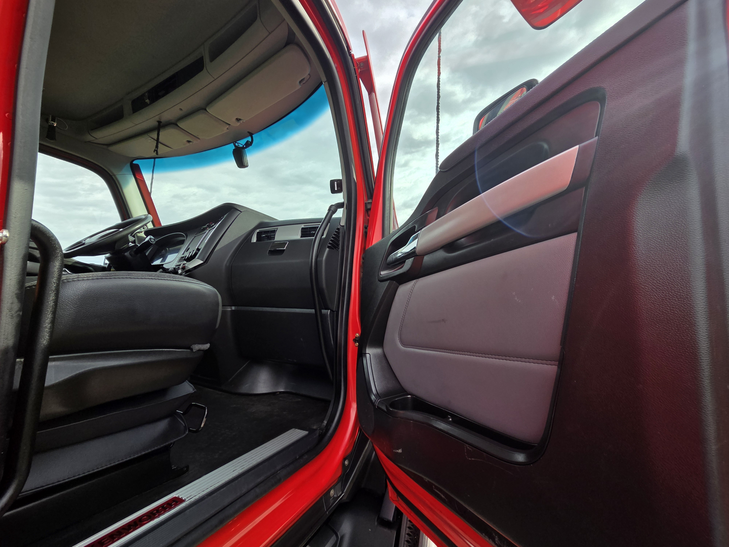 Kenworth T680 cab interior viewed from open driver door showing dashboard, steering wheel, and door panel.