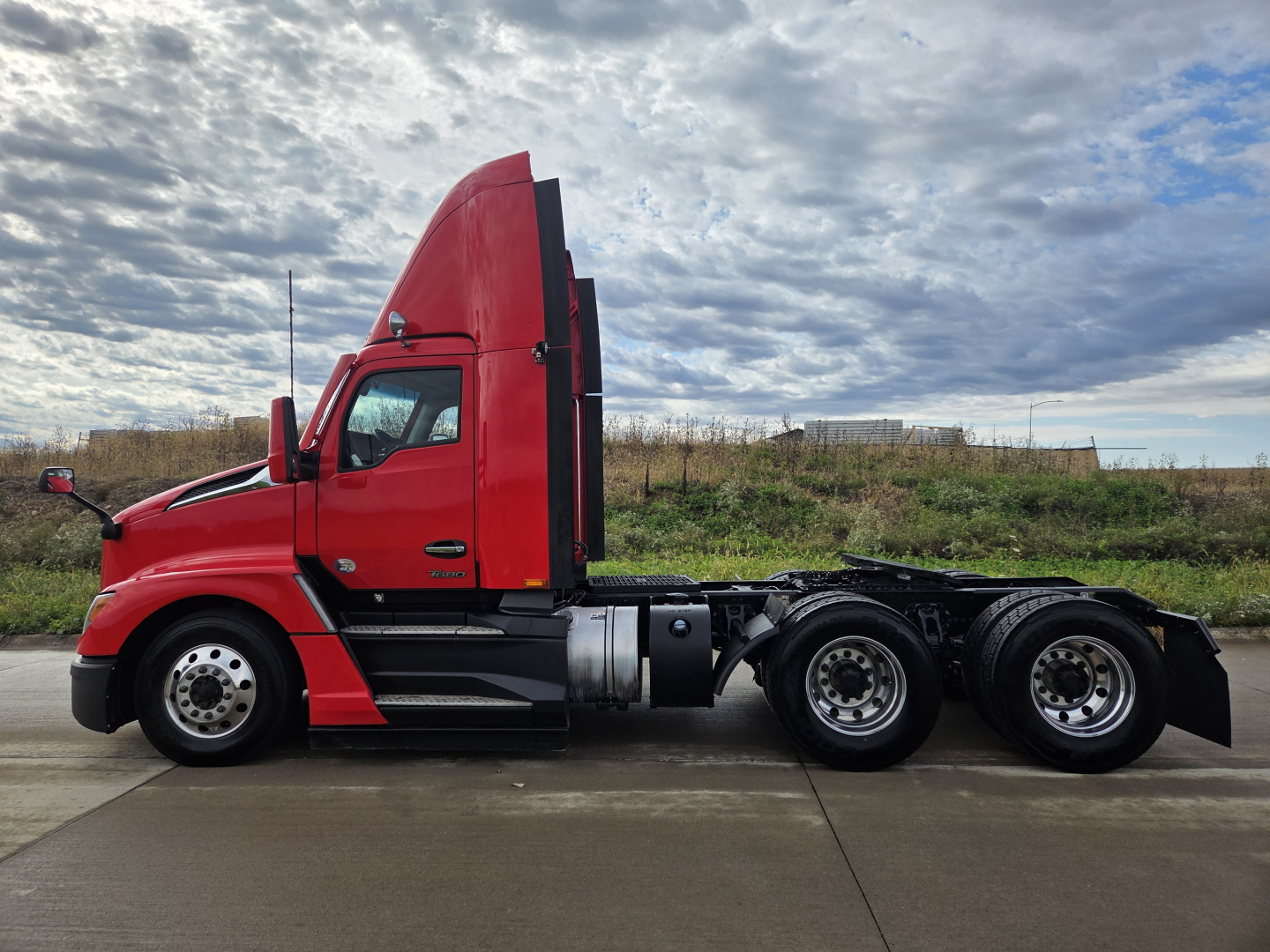 Kenworth T680 tractor-side view showing cab, hood, and dual rear axles with red paint and black chassis.