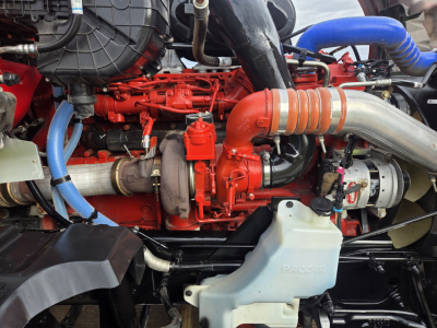 Kenworth T680 engine bay showing red engine components, blue hoses, and a large silver exhaustpipe with orange heat shield.