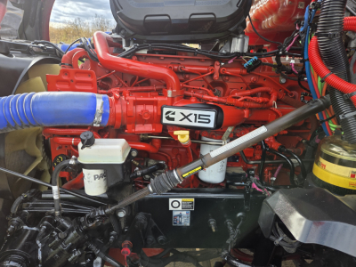 Kenworth T680 engine bay showing X15 badge, red engine block, blue intake hose, white reservoir, and various hoses and components.