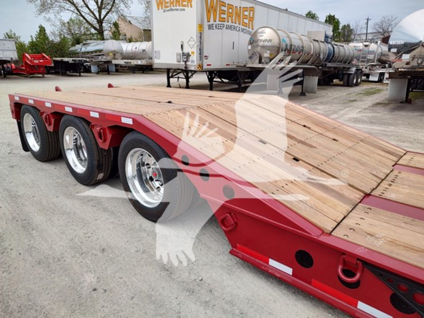  Fontaine lowboy trailer showing wooden deck and triple-axle configuration with red frame and polished alloy wheels.