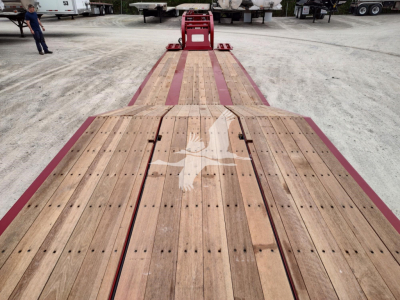 Flatbed trailer with wooden deck, red frame, and visible front A-frame hitch; long dual wooden planks with metal fasteners.