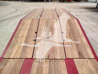 Flatbed trailer bed with wooden planks and red frame edges, long side boards, and metal fasteners; no visible signage or text on the deck.