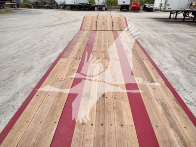 Flatbed trailer deck with wooden planks and maroon painted rails; no legible text visible on the surface in this view.