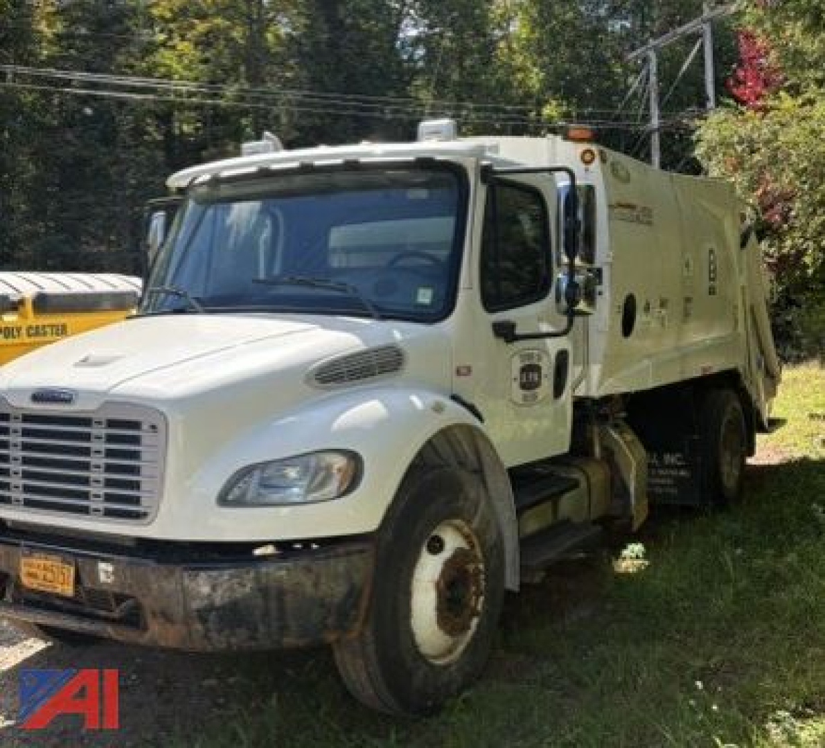 Truck front-left view showing white Freightliner M2 106 refuse collection body with bumper, grille, and wheel; company logos and side compartments visible.