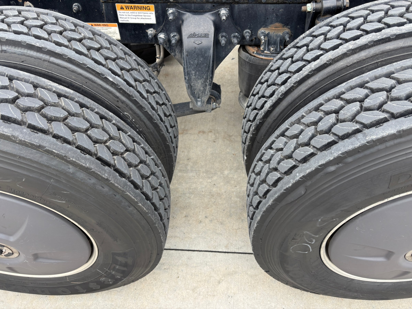 Dual rear truck wheels and suspension hitch seen from below on Freightliner PT126064ST; heavy-duty tires with tread and wheel rims visible; chassis crossmember in center.