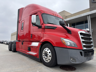 Truck cab of a red 2023 Freightliner PT126064ST shown from front-left angle with large grille and sleeper area.