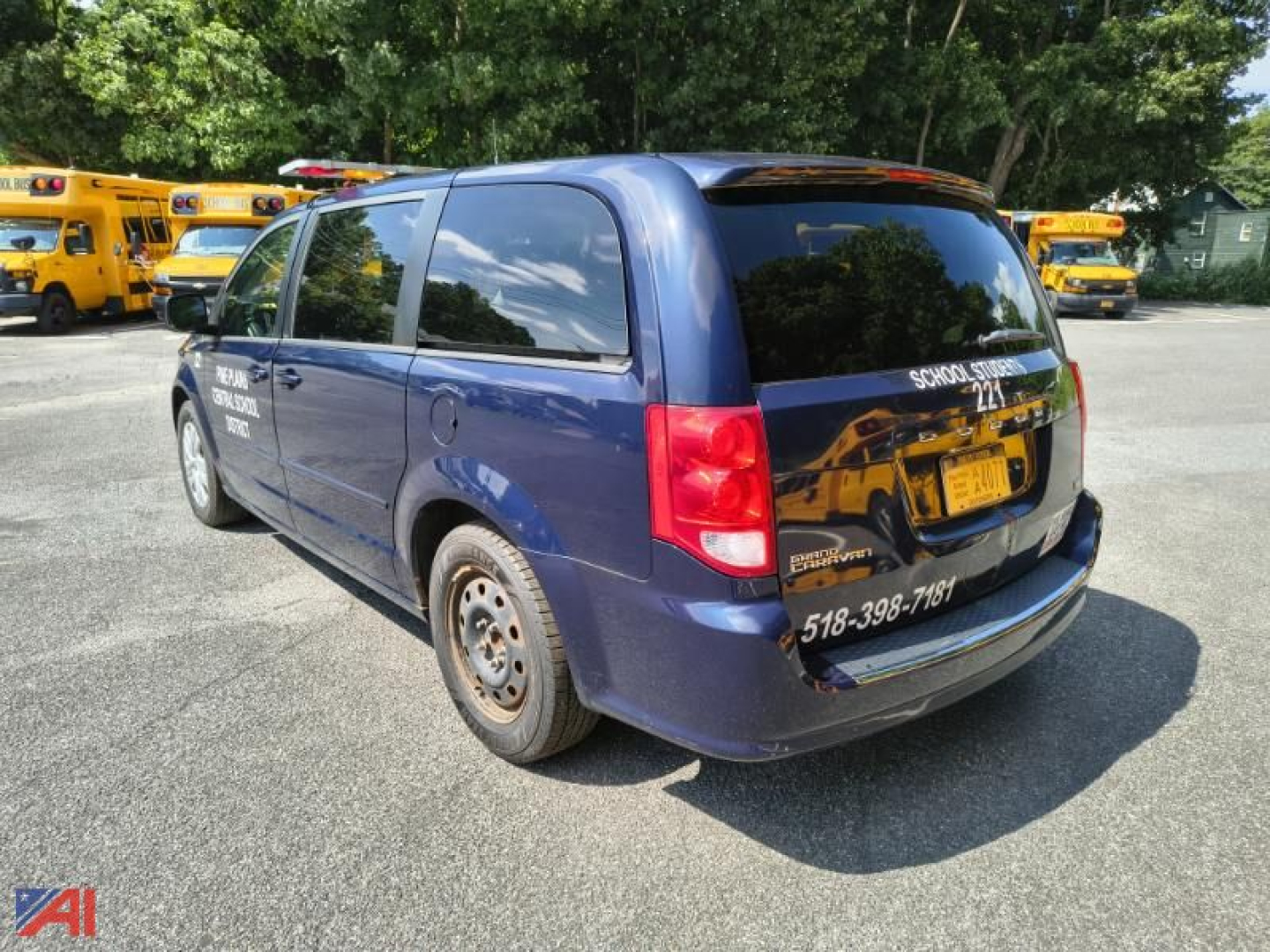 Dodge Grand Caravan minivan rear three-quarter view showing blue body, blacked-out rear window, tail lights, and a sticker with phone number on the bumper.