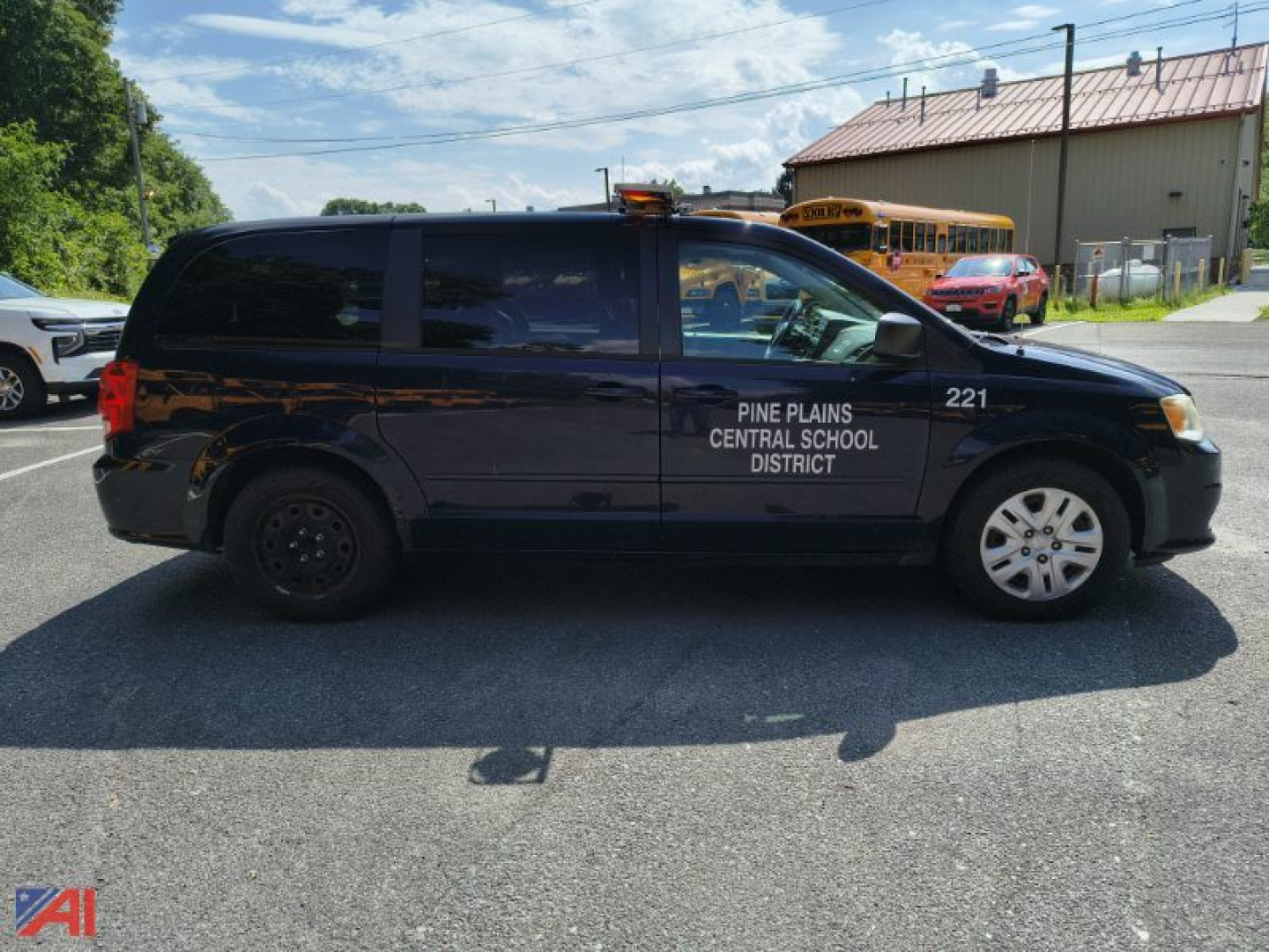 Side view of a black Dodge Grand Caravan police/administrative vehicle with Pine Plains Central School District text on front door, 2014 model, passenger van, with a school bus in background.