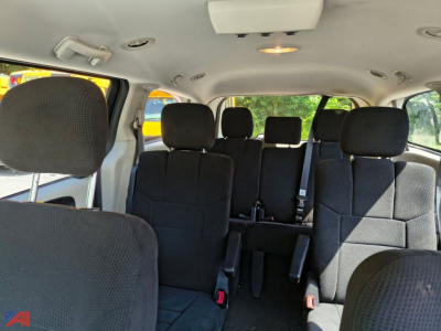 Interior of a 2014 Dodge Grand Caravan showing the second and third row seats in black fabric with headrests and a light over the center roof console.