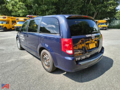 Dodge Grand Caravan minivan rear three-quarter view showing blue body, blacked-out rear window, tail lights, and a sticker with phone number on the bumper.