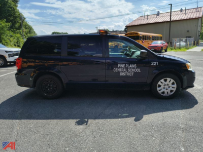 Side view of a black Dodge Grand Caravan police/administrative vehicle with Pine Plains Central School District text on front door, 2014 model, passenger van, with a school bus in background.