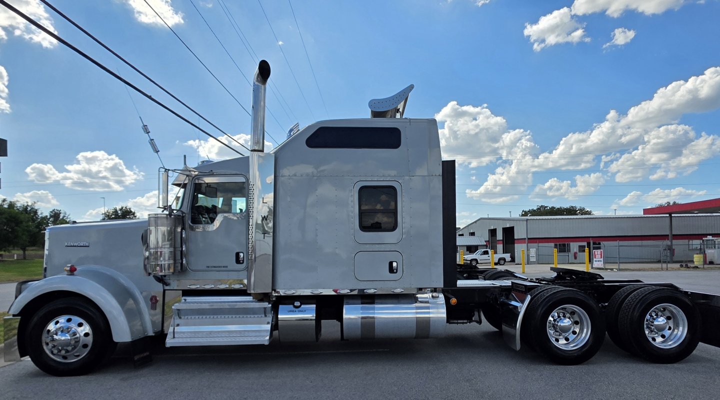 Kenworth W900 cab and chassis side view showing chrome fuel tanks, aluminum cab, large exhaust stack, and dual rear axles with tires.