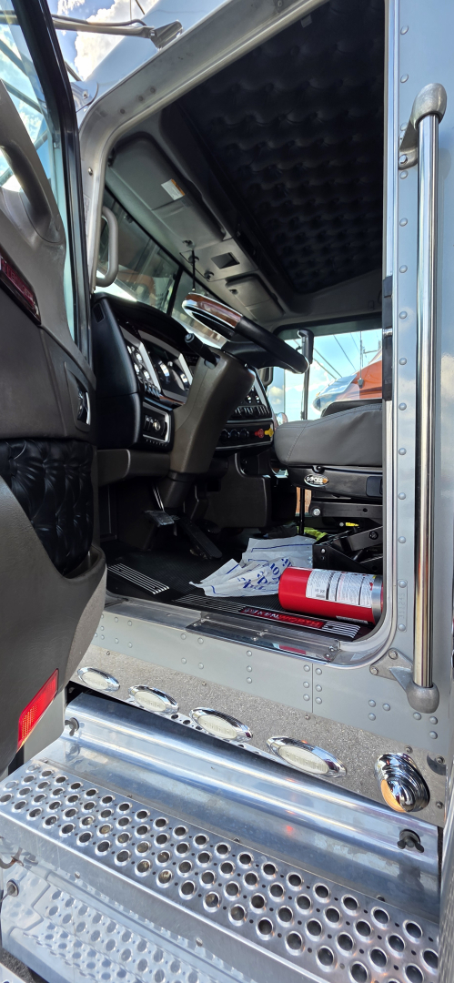 Kenworth W900 cab interior with steering column, dashboard, and entry step; metal door frame and perforated metal entry plate visible.