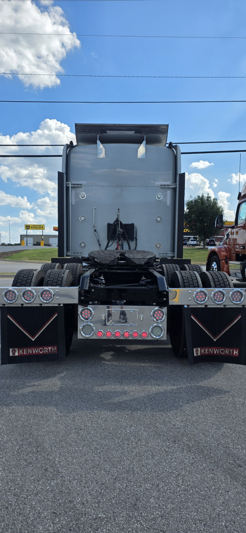 Kenworth W900 rear view showing chassis, dual rear axles, taillights, mud flaps with Kenworth branding, and a metallic cab-back with visible rear bumper and wheel wells.
