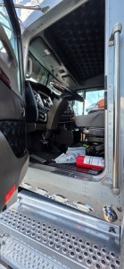 Kenworth W900 cab interior with steering column, dashboard, and entry step; metal door frame and perforated metal entry plate visible.