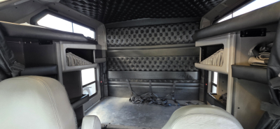Kenworth W900 cab interior cargo space with black diamond-plate back wall, overhead bunk shelves, and light gray seats, showing cabin area and storage compartments.